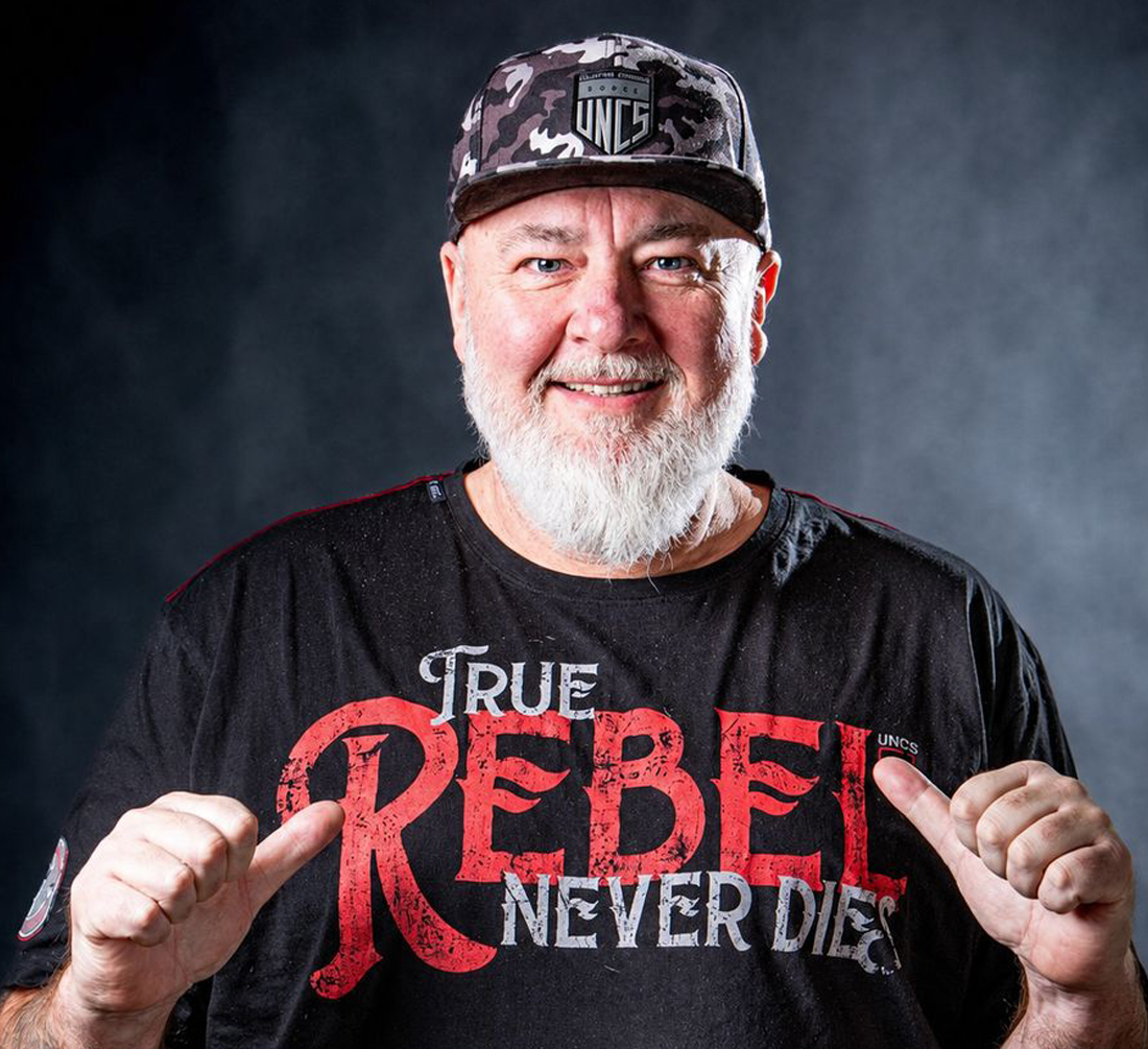 Tomáš v šiltovke a tričku True Rebel, s úsmevom ukazuje palcami na seba